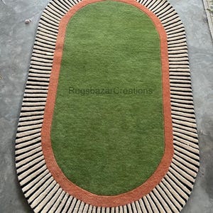 May include: Oval-shaped rug with a green center, bordered by a rust-colored band and a cream and black striped edge. The rug features the text "Rugsbazar Creations".