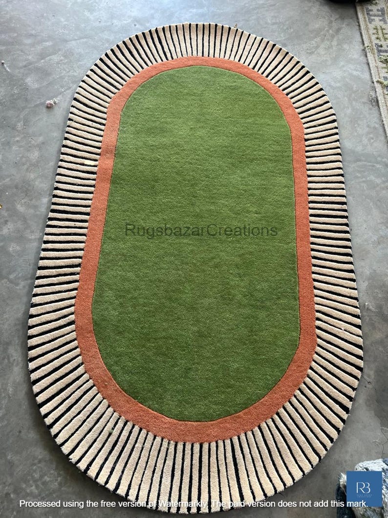 May include: Oval-shaped rug with a green center, bordered by a rust-colored band and a cream and black striped edge. The rug features the text "Rugsbazar Creations".