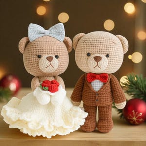 Könnte beinhalten: Zwei gehäkelte Teddybären, einer in einem weißen Kleid mit blauer Schleife und einem Strauß roter Rosen, der andere in einem braunen Anzug mit roter Fliege. Die Bären sind handgefertigt und haben ein Hochzeitsthema.