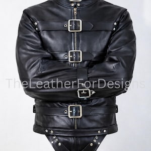 Puede incluir: Chaqueta de cuero negro con múltiples correas y hebillas. La chaqueta tiene un cuello alto y cierre de cremallera. Las mangas están diseñadas para cruzarse sobre el pecho y se aseguran con correas. La parte inferior está sujeta con una correa de entrepierna.