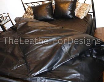 May include: A bed with black leather bedding, including a comforter and pillows. The pillows are square and shiny. The headboard is black metal with a decorative design. The text "TheLeatherForDesigns" is visible.