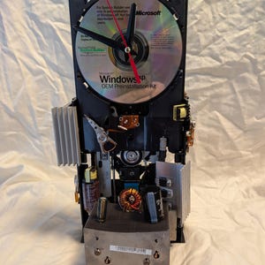 Puede incluir: Un reloj único construido con componentes de computadora, con un CD de Microsoft Windows XP como esfera. Las manecillas del reloj son negras con un segundero rojo. El reloj está hecho con varias piezas electrónicas.