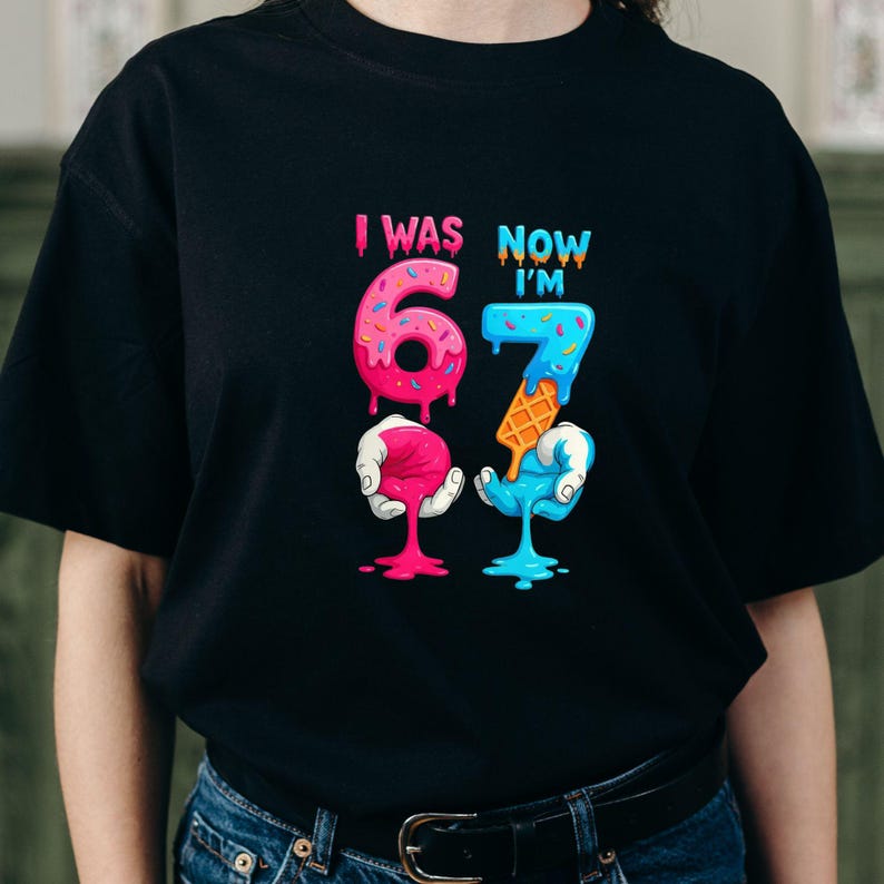 May include: Black t-shirt with a colorful graphic that reads "I WAS 6 NOW I'M 7". The numbers are designed to look like melting ice cream cones. The number 6 is pink and the number 7 is blue.