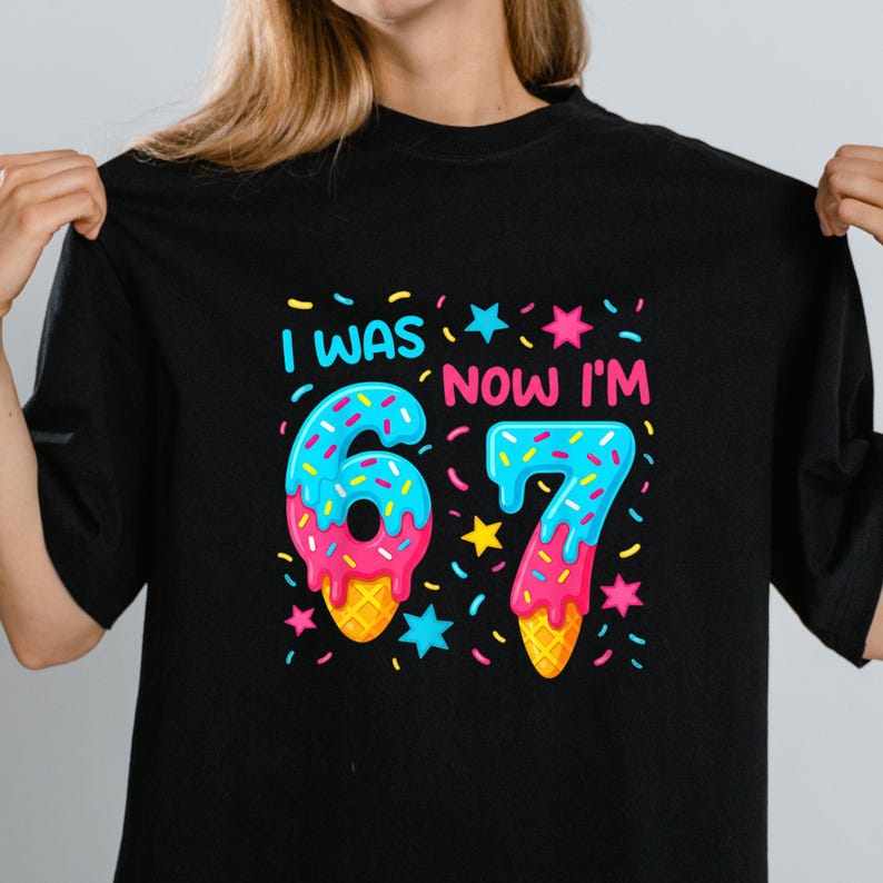 May include: Black t-shirt with a colorful graphic that says "I WAS 6, NOW I'M 7." The numbers are designed to look like ice cream cones with blue frosting and sprinkles. The design includes stars and confetti.