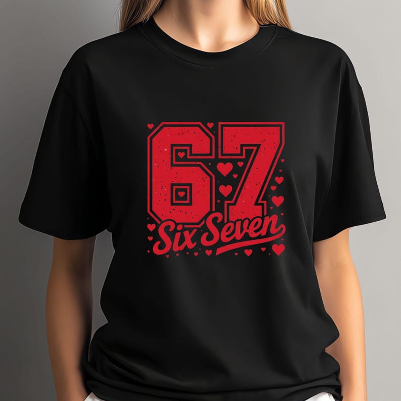May include: Black t-shirt with a red graphic design. The design features the number "67" in a collegiate style, with small hearts and the words "Six Seven" in a script font. The shirt is made of a soft material.