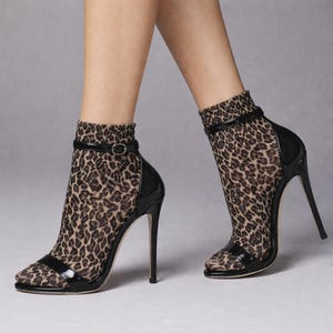 May include: Black and tan leopard print high-heeled ankle boots. The boots have a pointed toe and a thin, stiletto heel. A black strap with a small buckle secures the ankle. The upper part of the boot is made of a sheer leopard print fabric.