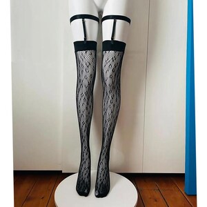 May include: Black fishnet thigh-high stockings featuring a subtle leopard print pattern. The stockings are held up by black garter straps that connect to a matching black elastic band worn around the upper thigh, creating a cohesive look.