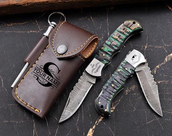 May include: A set of personalized knives with a brown leather sheath. The knives have patterned blades and green and black handles. The sheath is embossed with the text "YOUR NAME" and a decorative initial. A sharpening steel is also included.