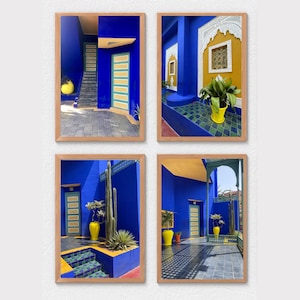 May include: Four framed prints featuring vibrant blue walls, yellow accents, and architectural details. Each print showcases a different view of a courtyard with stairs, doors, and potted plants. The frames are a light brown color.