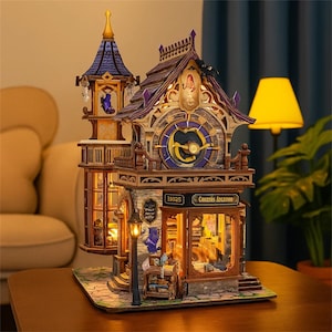May include: A detailed wooden model of a whimsical shop with a clock tower. The model features intricate details, including a clock face, a street lamp, and illuminated windows. The shop's sign reads "Comates Atgation".