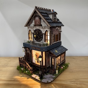 May include: A miniature Cuckoo House model with a detailed facade, featuring a clock face, windows, and a small balcony. The model has a dark gray roof, a black lamppost, and the text "Cuckoo House". The model is lit from within, creating a warm glow.