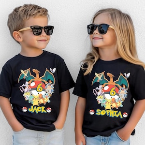 May include: Two children wearing black t-shirts with a colorful Pokemon graphic. The graphic includes a red and white Pokeball, various Pokemon characters, and the number 6. The shirts also have the names "Jack" and "Sophia" printed on them.