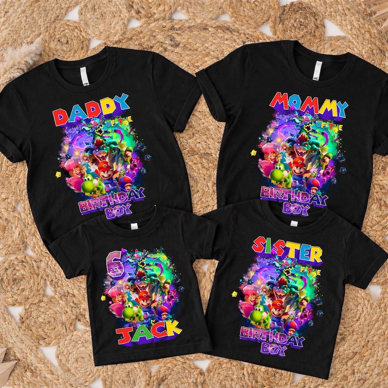 Pode incluir: Quatro camisetas pretas com designs gr&aacute;ficos coloridos. As camisas s&atilde;o rotuladas como "Daddy", "Mommy", "Sister" e "Jack", com um gr&aacute;fico de "Birthday Boy". As camisas est&atilde;o em uma superf&iacute;cie tecida.