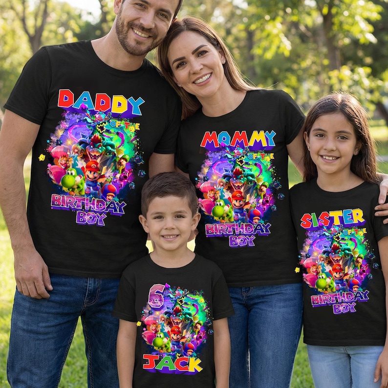 Pode incluir: Quatro camisetas pretas com gr&aacute;ficos coloridos e texto. As camisetas dizem "Daddy", "Mommy", "Sister" e "Jack". A camiseta "Jack" tamb&eacute;m tem o n&uacute;mero "6". Os gr&aacute;ficos apresentam personagens de videogame. A fam&iacute;lia est&aacute; sorrindo.