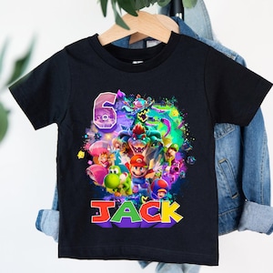 Pode incluir: T-shirt preto com um gr&aacute;fico colorido de personagens de videojogos, incluindo Mario, Yoshi e Bowser. O n&uacute;mero "6" e o nome "JACK" s&atilde;o exibidos em cores vibrantes, tornando-o uma t-shirt de anivers&aacute;rio perfeita.