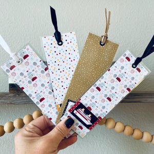 May include: Four decorative bookmarks with various patterns and ribbons. One bookmark features a cruise ship graphic. The patterns include colorful dots, gold with white dots, and a festive design with red and blue elements.