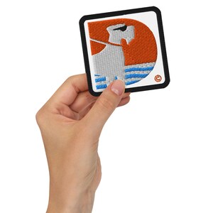 Peut inclure: Écusson brodé avec un motif stylisé d'une personne portant des lunettes de soleil, sur fond orange et rayures bleues. L'écusson a une bordure noire et un fond carré blanc. Le design est une représentation artistique unique.