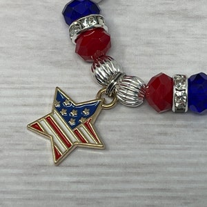 Pu&ograve; includere: Un braccialetto patriottico con perline rosse, bianche e blu e dettagli argentati. Un ciondolo a forma di stella dorata con il design della bandiera americana pende dal braccialetto. Il braccialetto &egrave; realizzato con perline sfaccettate ed elementi decorativi argentati.