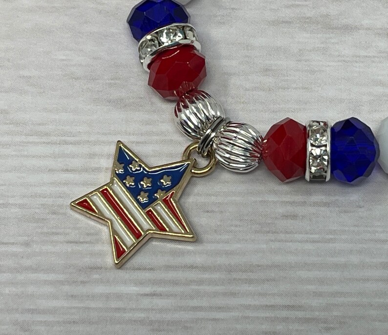 Pu&ograve; includere: Un braccialetto patriottico con perline rosse, bianche e blu e dettagli argentati. Un ciondolo a forma di stella dorata con il design della bandiera americana pende dal braccialetto. Il braccialetto &egrave; realizzato con perline sfaccettate ed elementi decorativi argentati.