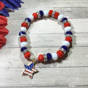 Pu&ograve; includere: Un braccialetto patriottico con perline rosse, bianche e blu, accentuato da distanziatori argentati. Un ciondolo a forma di stella dorata con un disegno della bandiera americana pende dal braccialetto. Il braccialetto &egrave; progettato per essere indossato al polso.
