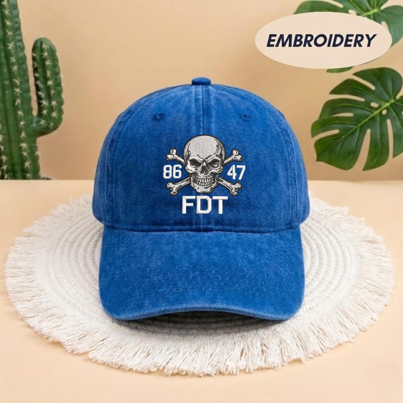 Puede incluir: Una gorra de b&eacute;isbol azul con acabado desgastado que presenta un gr&aacute;fico bordado en blanco de una calavera con tibias cruzadas. El dise&ntilde;o incluye los n&uacute;meros 86 y 47 a ambos lados de la calavera, con las letras FDT impresas en blanco debajo.