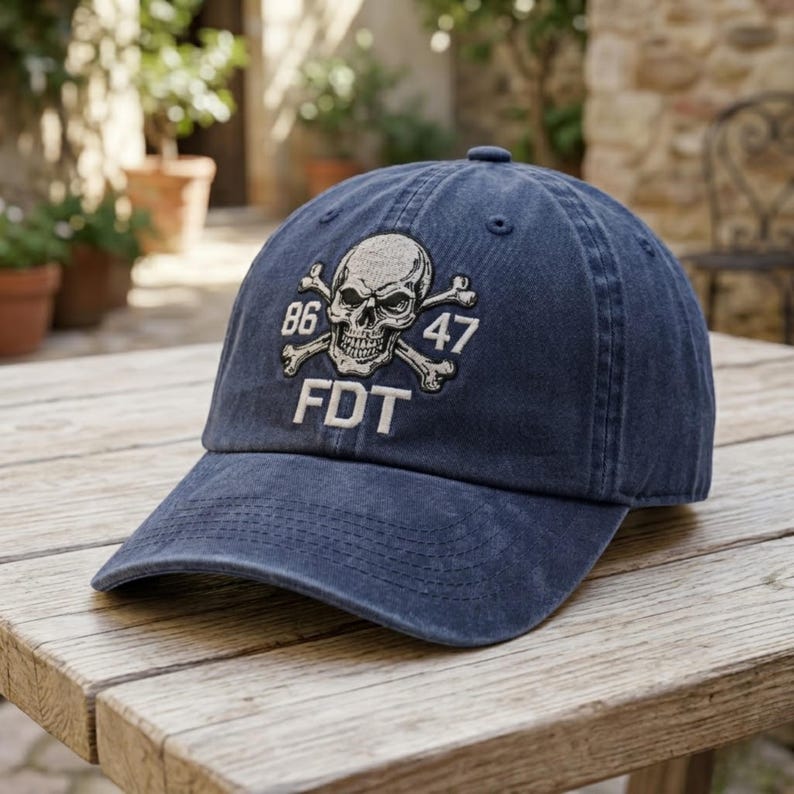 Puede incluir: Una gorra de b&eacute;isbol azul marino con un gr&aacute;fico bordado de una calavera y tibias cruzadas. Los n&uacute;meros 86 y 47 est&aacute;n cosidos a ambos lados de la calavera, con las letras FDT bordadas en hilo blanco justo debajo del dise&ntilde;o.