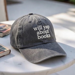May include: A gray baseball cap with the phrase "will yap about books" embroidered in white. The cap has a curved brim and a classic six-panel design. The hat is made of a soft, worn material.