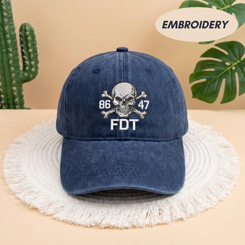 Puede incluir: Una gorra de b&eacute;isbol de mezclilla azul oscuro con un dise&ntilde;o bordado en blanco de una calavera y tibias cruzadas en la parte frontal. El bordado incluye los n&uacute;meros 86 y 47 a ambos lados de la calavera, con las letras FDT en blanco debajo.
