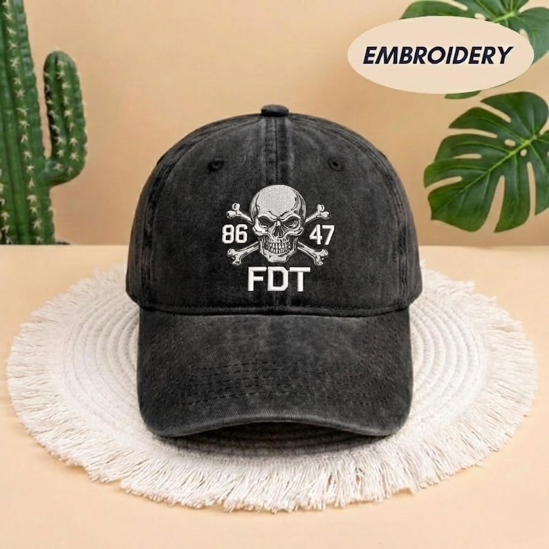 Puede incluir: Una gorra de b&eacute;isbol de algod&oacute;n lavado en color gris carb&oacute;n con un bordado blanco de una calavera y tibias cruzadas. El dise&ntilde;o incluye los n&uacute;meros 86 y 47 a ambos lados de la calavera, con las letras FDT impresas en blanco bajo los huesos.