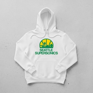 May include: White hoodie featuring a green and yellow Seattle Supersonics logo. The logo depicts the Space Needle and a cityscape. The hoodie has a drawstring hood and a front pocket. A comfortable sweatshirt for fans.