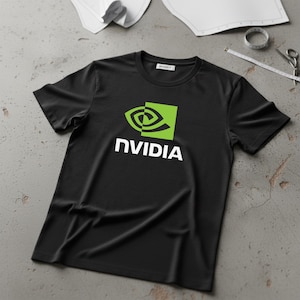 Puede incluir: Camiseta negra con el logotipo de NVIDIA en verde y blanco. El logotipo es un ojo estilizado dentro de un cuadrado verde, con la palabra "NVIDIA" debajo en blanco. La camiseta es de material suave y se muestra sobre una superficie gris.
