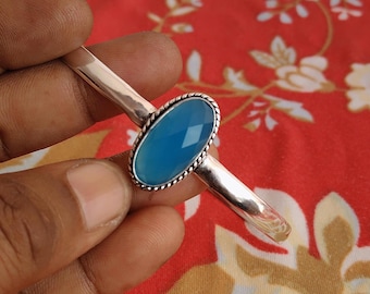 May include: A silver bracelet with an oval, faceted, light blue gemstone. The gemstone is set in a decorative bezel with a twisted rope design. The bracelet has a simple, polished band.