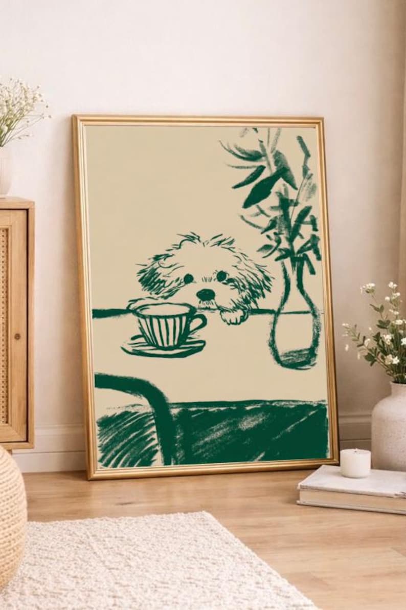 May include: A framed art print featuring a green and beige illustration. The artwork depicts a dog resting its head on a table with a teacup and saucer. A vase with greenery is also on the table. The print has a gold frame and is leaning against a wall.