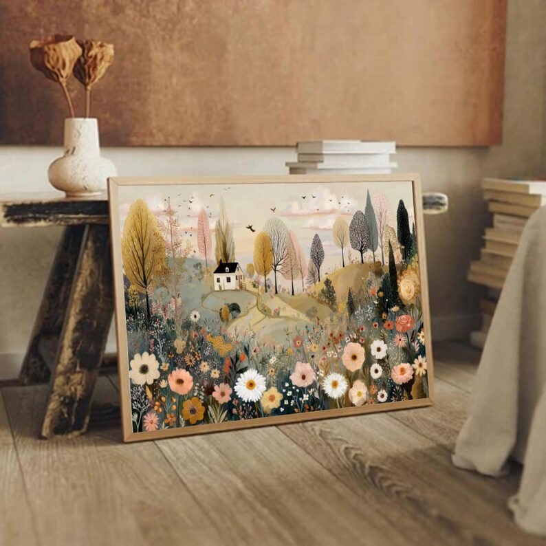 以下が含まれることがあります： 小さな白い家、木々、色とりどりの花が咲く野原が描かれた、額入りの風景画プリント。暖色系の色使いで、黄色、ピンク、緑色が使われています。