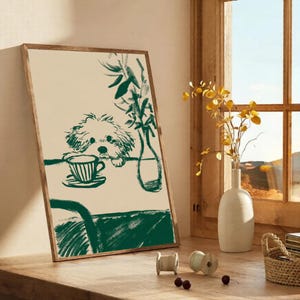 May include: A framed art print featuring a green sketch of a dog looking at a teacup and saucer on a table. A vase with greenery is also on the table. The artwork has a neutral background and a wooden frame.