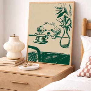 May include: A framed art print featuring a green sketch of a dog peering over a table with a teacup. The artwork is in a wooden frame and is displayed on a light-colored wall. A bedside table with a lamp and decorative items is in the foreground.