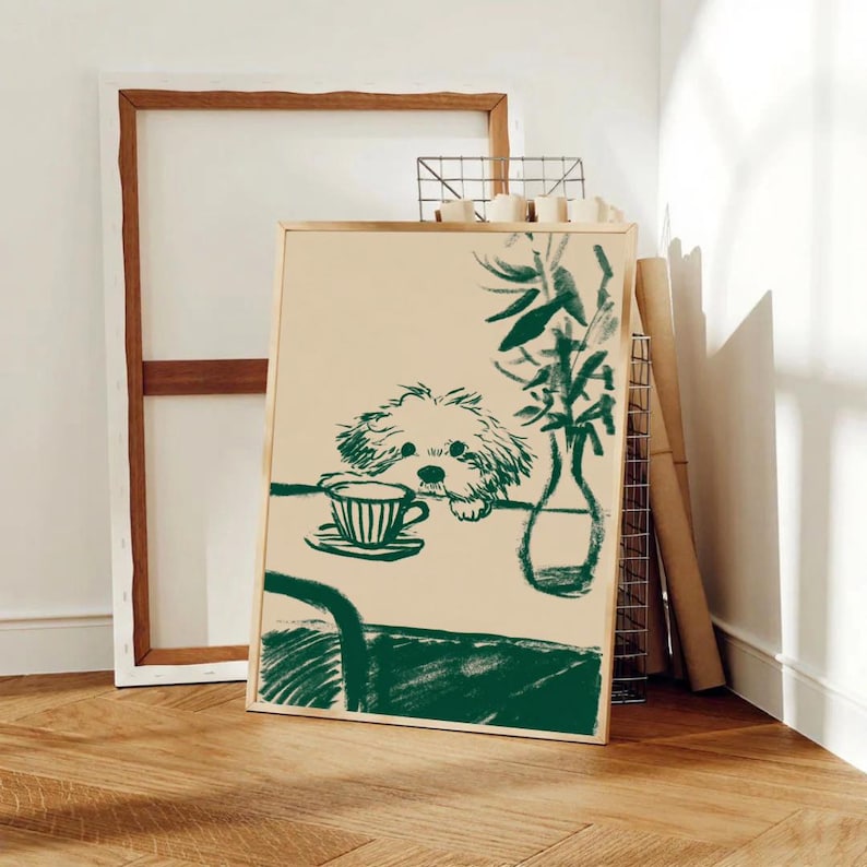 May include: A framed art print featuring a green sketch of a dog peering over a table with a teacup and vase. The artwork has a beige background and is set against a white wall and wooden floor.