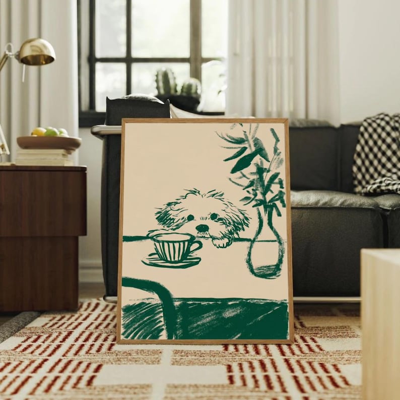 May include: A framed art print featuring a green and beige illustration. The artwork depicts a dog looking at a teacup on a table, with a vase of greenery. The print is in a wooden frame and is displayed in a living room setting.