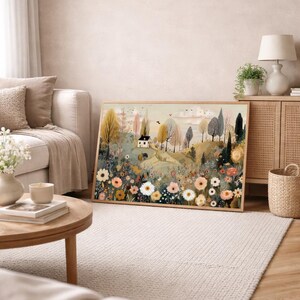 以下が含まれることがあります： 小さな白い家、木々、色とりどりの花が描かれた、額入りの風景画プリント。 リビングルームに飾られており、壁に立てかけられています。
