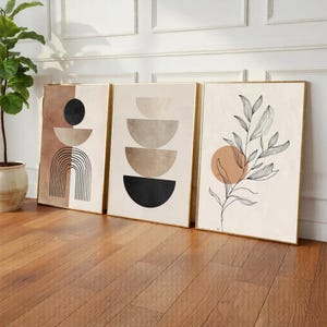 May include: Three framed abstract art prints. The prints feature geometric shapes, including arches, semi-circles, and a botanical design with a circular accent. The color palette includes beige, brown, black, and gold.