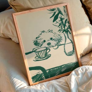 May include: A framed print featuring a green illustration of a dog peering over a table with a teacup. The artwork has a minimalist style, with a light beige background and a wooden frame. The dog is drawn in a loose, sketchy style.