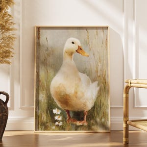 May include: A framed print featuring a white duck with a yellow beak and orange feet. The duck is depicted in a field of grass and wildflowers. The artwork has a vintage, rustic style, with a soft, muted colour palette.
