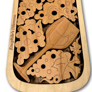 Könnte beinhalten: Ein Weinflaschenpuzzle aus Holz mit einem Weinglas und Weintrauben, die ausgeschnitten sind. Das Puzzle ist aus hellbraunem Holz gefertigt und hat die Worte "Enophile's Dilemma" auf der Seite eingraviert.