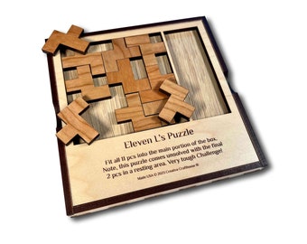 May include: A wooden puzzle box with the text "Eleven L's Puzzle" and instructions to fit all 11 pieces into the main portion of the box. The puzzle comes unsolved with the final 2 pieces in a resting area. The box is made in the USA by Creative Crafthouse.
