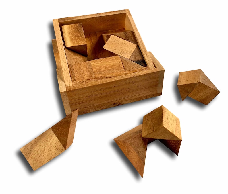 May include: A wooden puzzle box with a lid open, revealing a set of wooden puzzle pieces. The pieces are scattered around the box, some inside and some outside. The puzzle pieces are made of light brown wood and have various shapes and sizes.