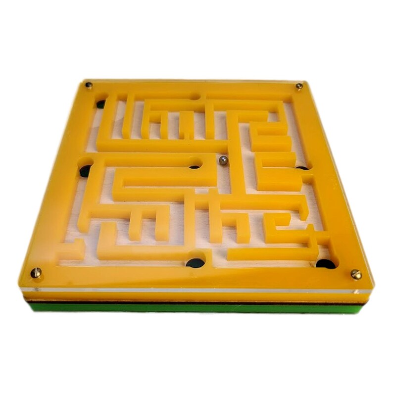 May include: A yellow maze game with a metal ball inside. The maze is made of a clear, yellow plastic and has a rectangular shape. The base of the game is green and white. The game is designed to challenge the player to navigate the ball through the maze.