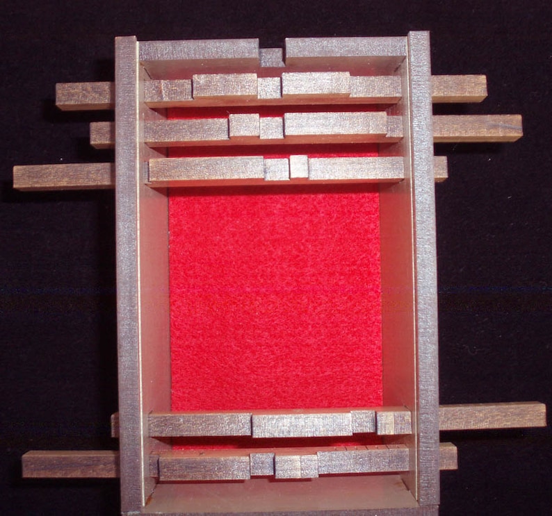 May include: A wooden box with a red felt lining and a series of wooden slats that can be moved around. The box is closed and the slats are in a random configuration.