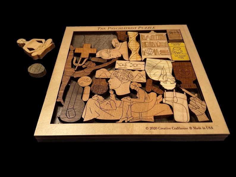 May include: The Psychiatrist Puzzle is a wooden jigsaw puzzle with a variety of shapes and designs. The puzzle features a psychiatrist and patient, as well as other symbols related to mental health. The puzzle is made in the USA. &copy; 2020 Creative Crafthouse.