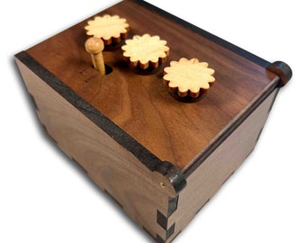 May include: A wooden puzzle box with three round knobs on the top. The box is made of walnut wood and has a dark brown stain. The knobs are made of light wood and have a decorative pattern.