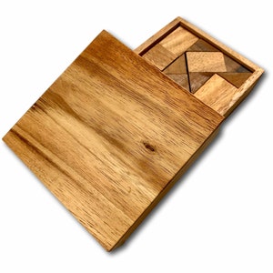 May include: A wooden box with a sliding lid, revealing a wooden puzzle with various geometric shapes. The puzzle pieces are made of light and dark wood, creating a contrasting pattern.